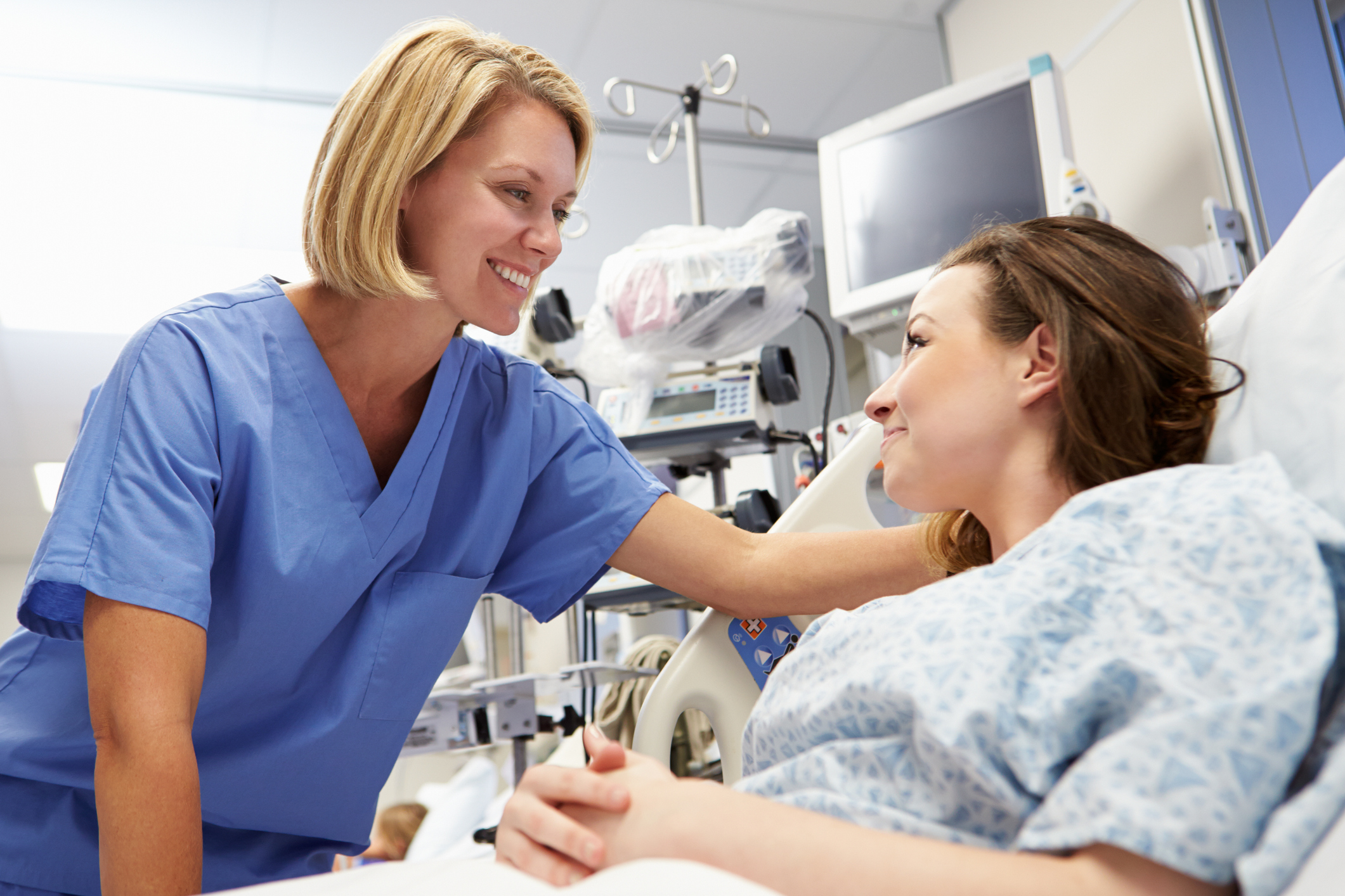 A nurse standing over patient while they both exchange cheerful smiles.