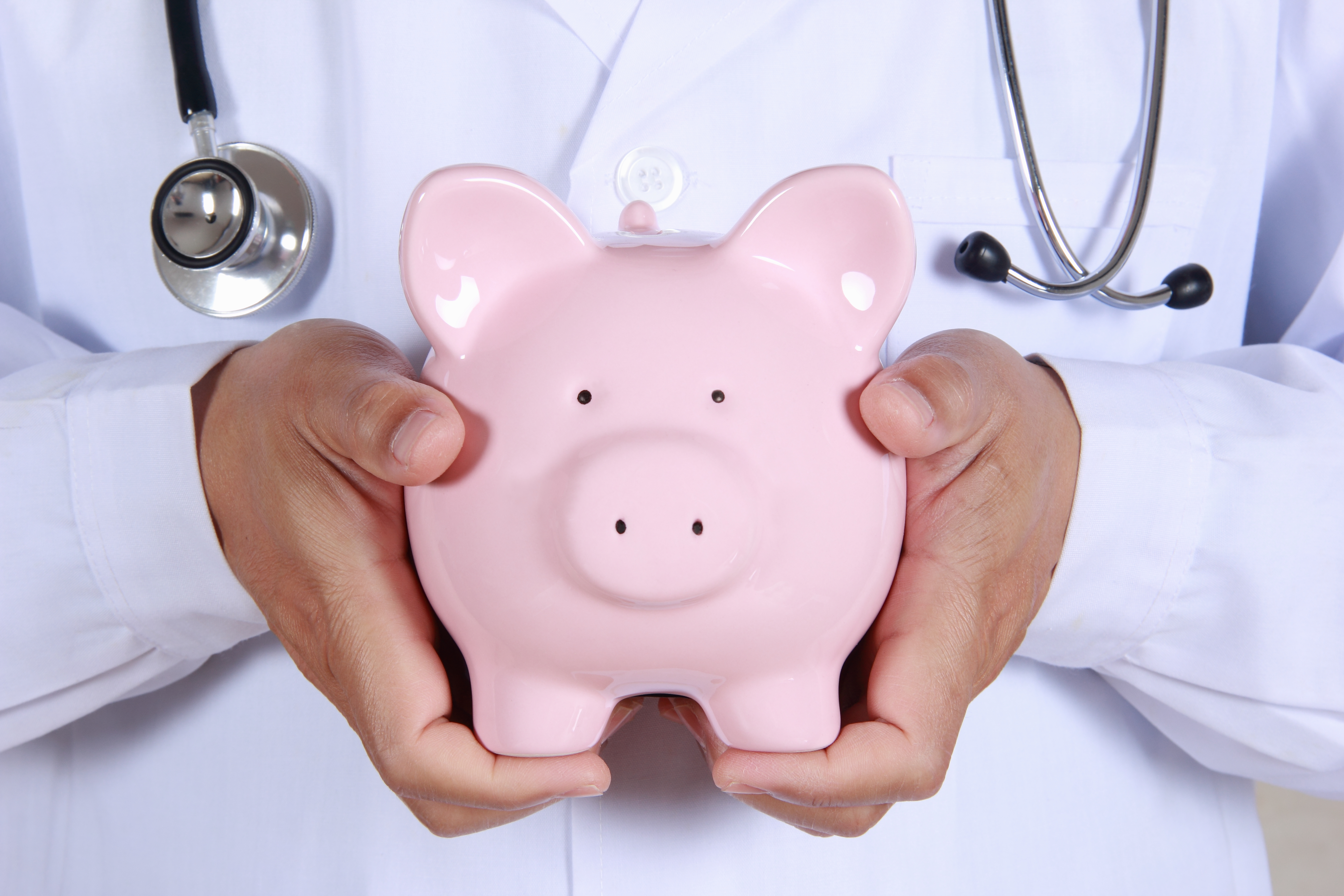 A person wearing a stethoscope holds a pink piggy bank.