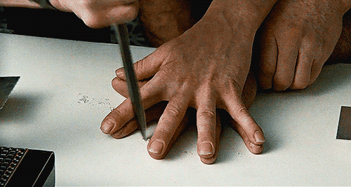 Two hands lay atop each other while a knife is jabbed between each finger.