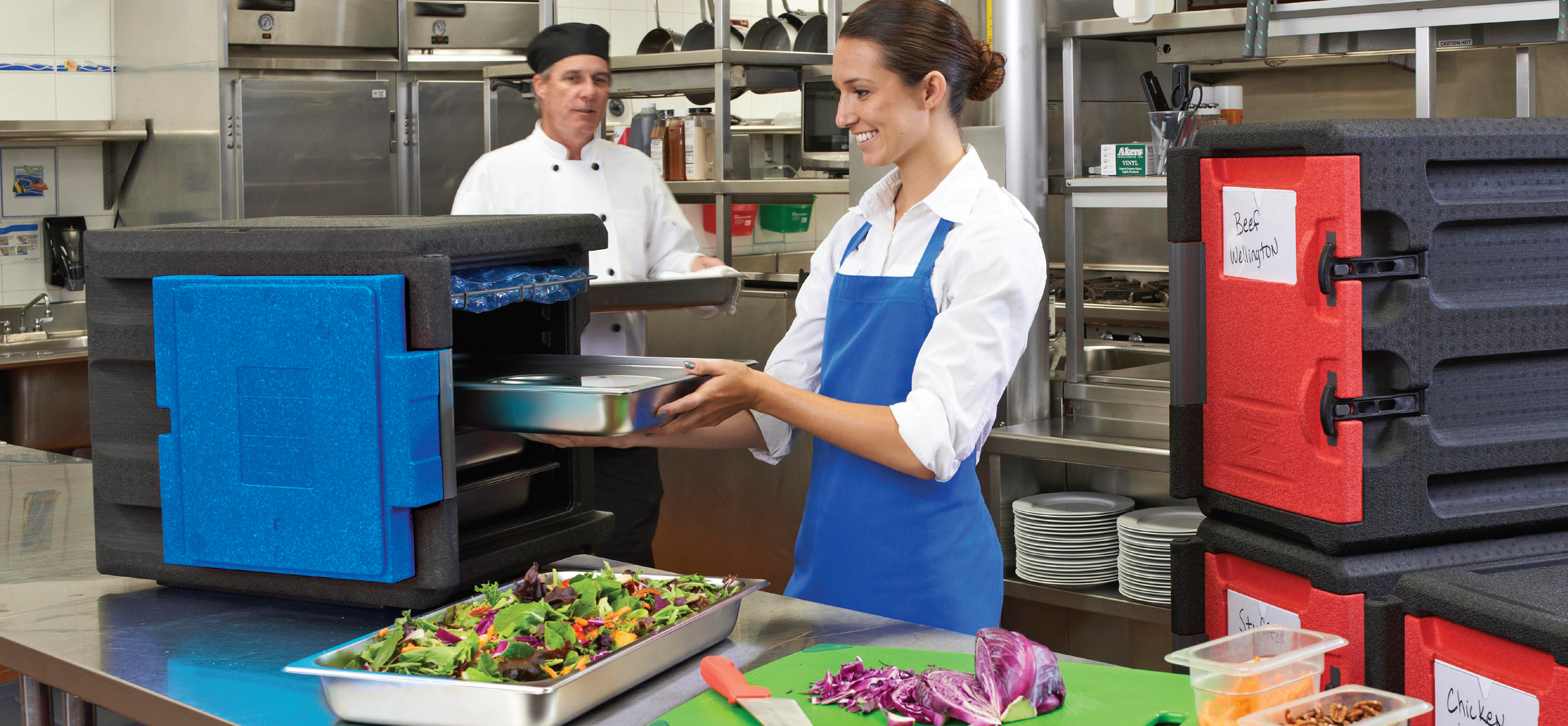 A woman standing behind food prep table, stores a food tray inside of the Mightylite.