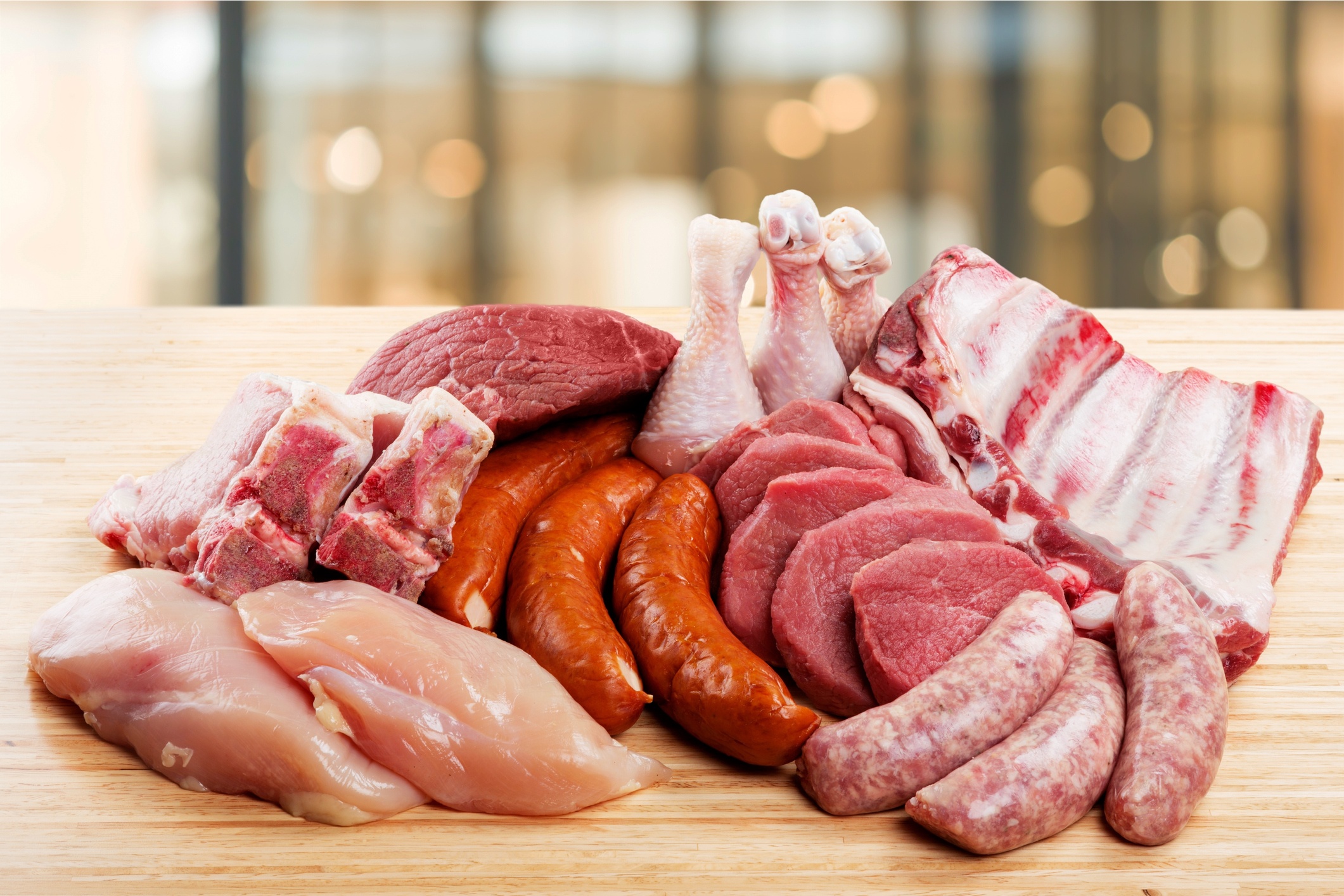 A variety of meats are gathered atop a wooden table.